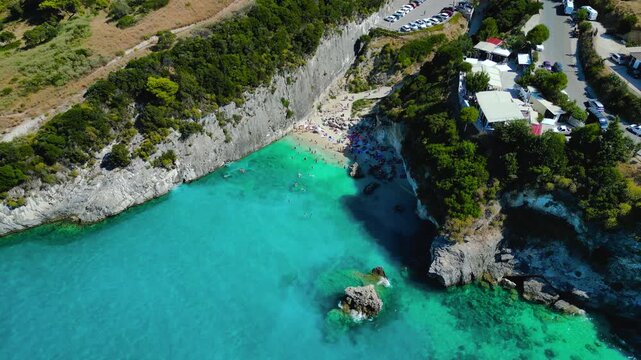Drone tilt-up reveals turquoise sulfur cove at Xigia Beach, Zakynthos. Crystal clear water, white cliffs, pine forest.