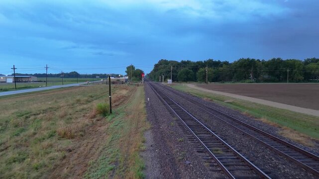 A drone tracks beside a freight train as it rolls past on rural tracks then slowly pulls away to reveal the empty rails fading into the darkening evening dusk sky.