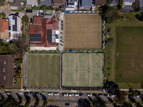 Football field, tennis courts, lawn bowling greens and houses in suburbia from top down aerial view on sunny day. 
