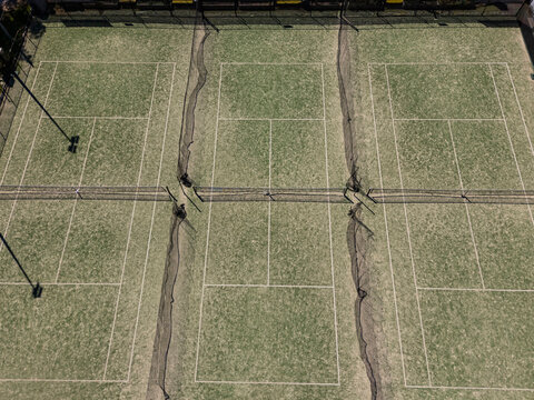 Artificial grass tennis courts from aerial view on sunny day with road visible in background.