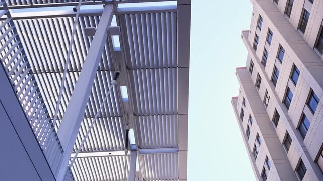 Smooth low-angle view while walking under a modern architectural canopy, revealing the exterior facade of a tall building at the University of California, Berkeley against a clear sky