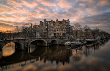 Obraz premium Amsterdam canal at sunset with historic bridge and houseboats reflecting in calm water