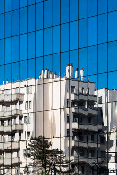 Residential building reflected in a blue glass facade creates a layered urban architectural detail contrasting old housing and modern surfaces