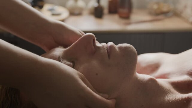 Young adult Caucasian man receiving relaxing facial massage therapy in beauty salon. Suitable for male skincare marketing, wellness campaigns, and aesthetic cosmetology videos