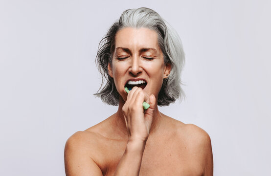 Woman brushing her teeth with eyes closed in studio