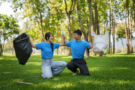 Asian volunteers high-fiving while cleaning up trash in park