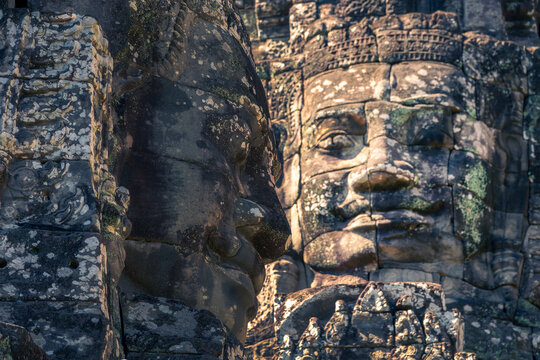 Close up of two giant stone faces at Bayon temple, side and frontal view in Angkor, Siem Reap, Cambodia