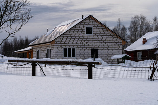 Quiet rural scene. Brick house covered in snow. Snow blankets the fence and yard. Bare trees stand in the background. Perfect for winter themes or countryside photography. Use in stories about peace