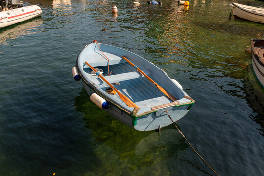 Traditional small boat floating in the clear green water of Portofino harbor, with colorful historic waterfront buildings and Mediterranean vegetation in Liguria, Italy.
