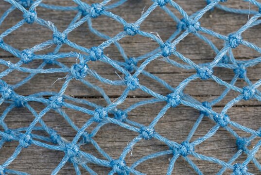 Blue nylon fishing net with knotted mesh pattern. Close up of woven maritime netting laid on weathered wooden boat deck