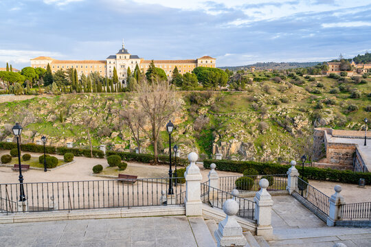View of a historic building perched on a rocky hill overlooking a valley with stone stairs and railings in the foreground in Toledo, Castile-La Mancha, Spain.