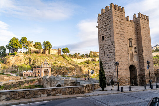 View of the historic Puerta de Alcantara stone gate and bridge with surrounding hillside and trees in Toledo, Castile-La Mancha, Spain.