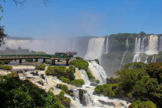 View of Iguazu Falls with a wooden observation deck filled with tourists, surrounded by lush tropical vegetation and cascading water in Foz do Iguacu, Parana, Brazil.