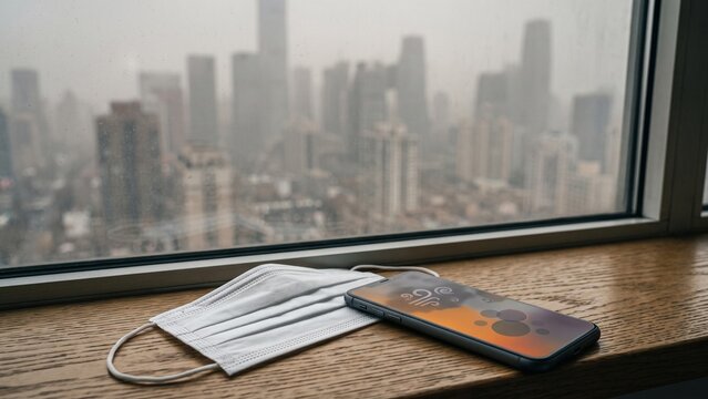 Medical Face Mask and Smartphone Showing Air Pollution Index on Window Sill
