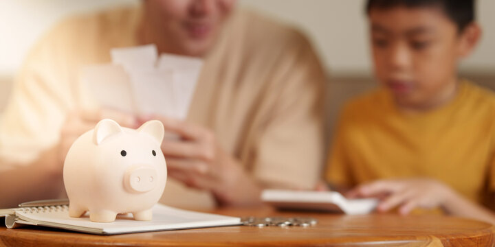 Piggy bank on desk with father and son calculating family budget in background