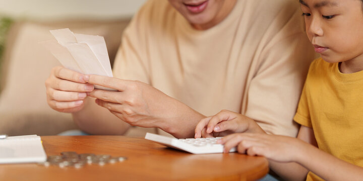 Asian father and son calculating expenses with receipts and calculator for family budget