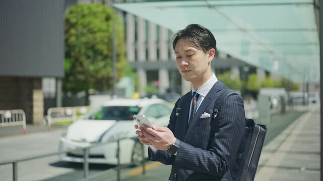 Japanese businessman using a ride hailing app on a city street