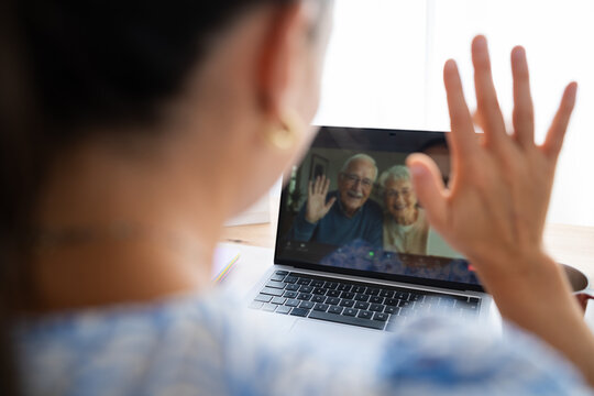 Elderly couple waving during video call on laptop at home office