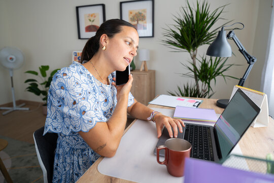 White woman telecommuting at home office desk with laptop and phone