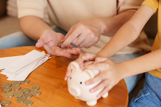 Cropped hands of parent and child putting coins into piggy bank for financial savings