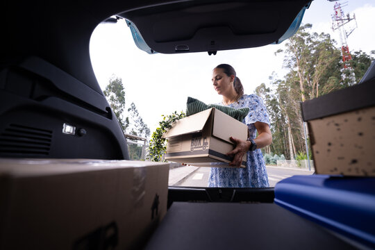 White woman loading moving box into car trunk outdoors