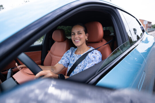 White woman smiling while driving a blue car with leather seats