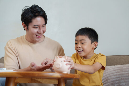 Happy Asian father and son putting money in piggy bank for future financial literacy