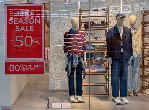 Cartel Mid Season Sale -50% en escaparate con maniqu&iacute;es con ropa estilo Denim + Stripes, de una tienda de ropa Springfield en Madrid, Espa&ntilde;a, 16 de septiembre de 2026