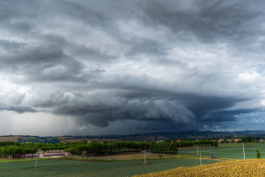 View of a dramatic storm front with dark, heavy clouds looming over the rural landscape of fields and trees in Corridonia, Marche, Italy.