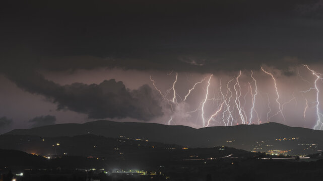 View of multiple lightning bolts striking over the dark hills at night near Corridonia, Marche, Italy.