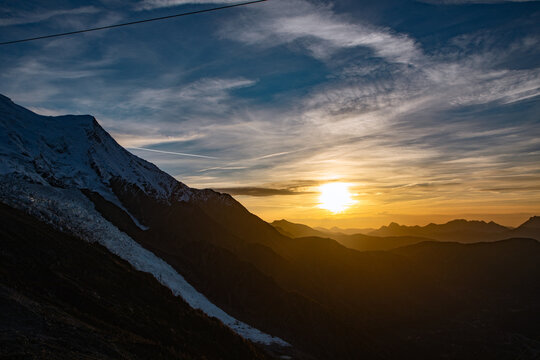 View of the snow-capped peak of Mont Blanc at sunset with dramatic clouds and golden light over the mountain range in Chamonix, Auvergne-Rhone-Alpes, France.
