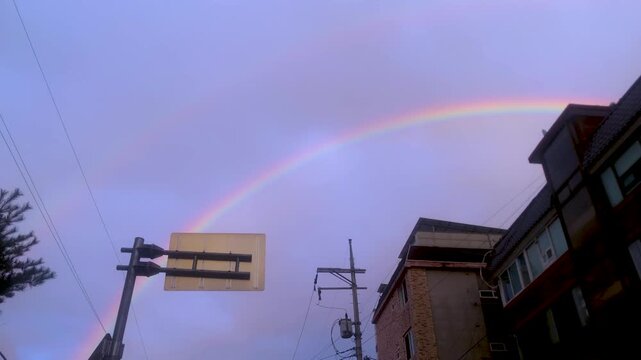Rainbow appears over an urban skyline and power lines after rain.