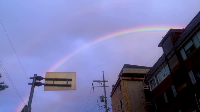 Rainbow appears over an urban skyline and power lines after rain.