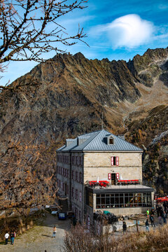View of a stone mountain refuge with red shutters and a terrace set against the dramatic backdrop of the Mont Blanc massif in Chamonix, Auvergne-Rhone-Alpes, France.