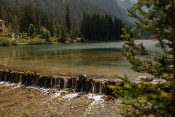 Small natural cascade flowing from Toblacher See, surrounded by coniferous forest and mountain scenery in the Italian Dolomites. © Viktoriia