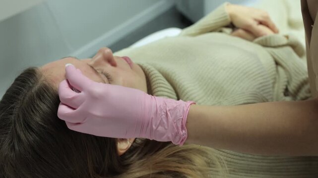 A gloved cosmetologist holds a syringe and injects filler into a client's forehead during a facial cosmetic procedure, top-down view