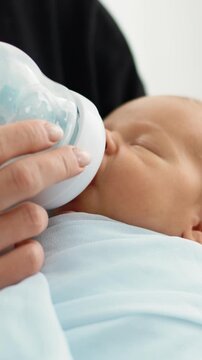 Close-Up Of A Newborn Eating From A Bottle In The Mother's Arms In Vertical Video