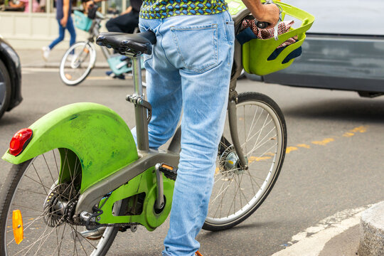 Man riding a shared bicycle with a green basket on an urban street, representing sustainable transportation, cycling culture and environmentally friendly mobility
