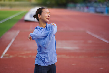Fototapeta premium Asian woman stretching arms on running track, preparing for outdoor workout, embracing fitness, healthy lifestyle, and wellbeing, finding motivation for daily exercise