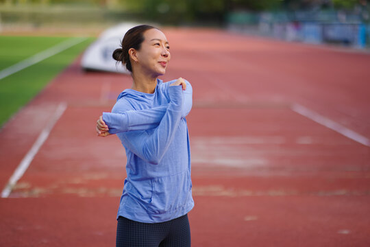 Asian woman stretching arms on running track, preparing for outdoor workout, embracing fitness, healthy lifestyle, and wellbeing, finding motivation for daily exercise