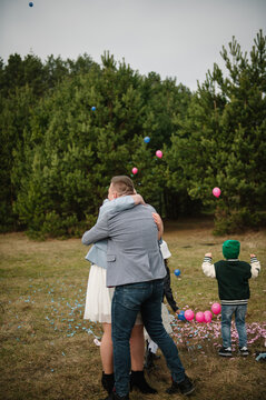 Loving couple hugging each other tenderly with children nearby during a twin gender reveal celebration in a forest.