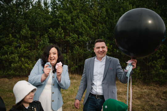 Happy pregnant woman and her smiling husband with their two cute children laughing during a fun gender reveal celebration in a forest.