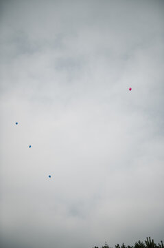Small blue and pink balloons floating high up in the cloudy sky after a twin gender reveal celebration.