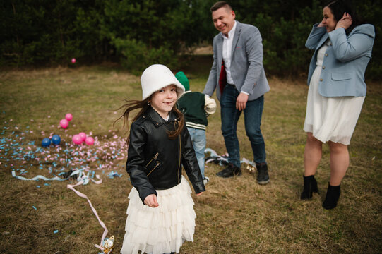 Cute little girl smiling and running away from confetti during a twin gender reveal celebration outdoors in a forest.