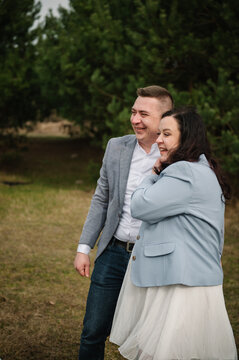 Happy expecting parents smiling and laughing together outdoors in a forest during a twin gender reveal photo session.