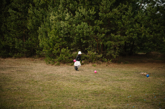 Little girl running and playing with small balloons on a clearing in a pine forest during a family outdoor celebration.