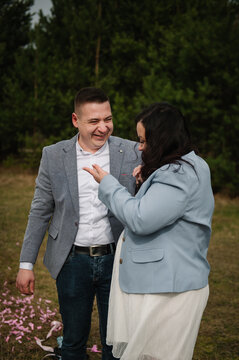 Happy expecting parents smiling and talking joyfully outdoors in a forest during a twin gender reveal photo shoot.
