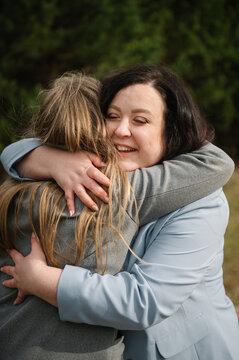 Two happy women embracing each other warmly outdoors in a park, celebrating a special holiday or birthday.