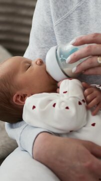 Close-Up Of A Newborn Eating From A Bottle In The Mother's Arms In Vertical Video