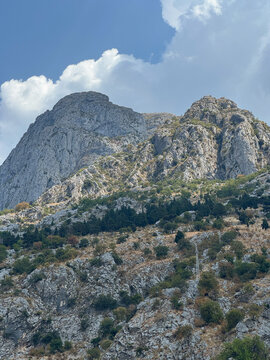 Steep, rugged limestone mountain peak rises into a blue sky with soft white clouds
